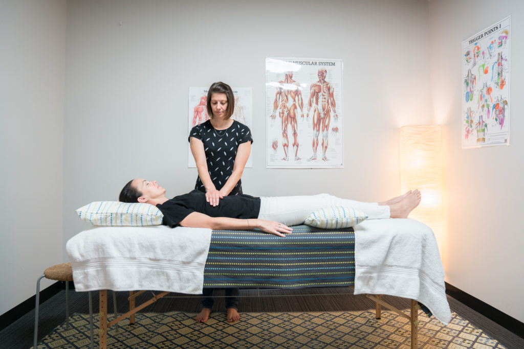 An image of a reiki treatment with a person on the treatment table and Amy holding hands on torso