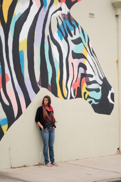 Amy B, Reiki teacher, leaning against a wall next to a zebra painting in Fremantle