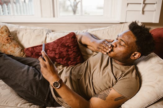 Man lying on a couch using smartphone for video call at home, appearing relaxed and connected.