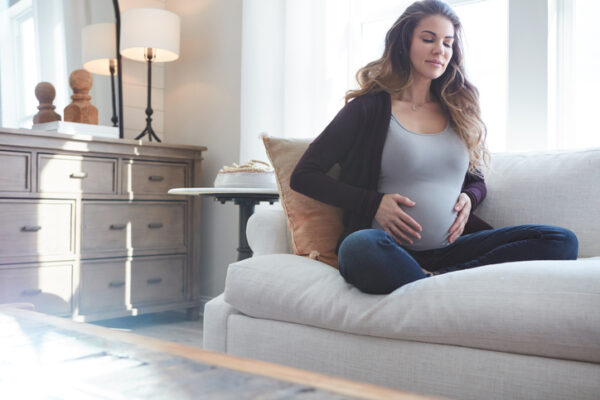 Pregnant woman sitting on sofa giving herself Reiki