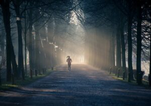 A woman running along a misty, tree-lined path at sunrise, symbolizing the morning meditation that inspired Reiki Mass.